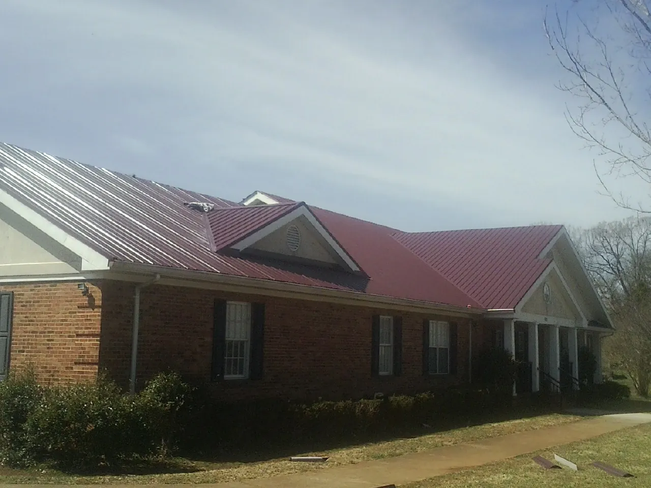 Red metal roof with gabled entries on a long brick building, from a Hail Damage Roof Repair job in Smartsville