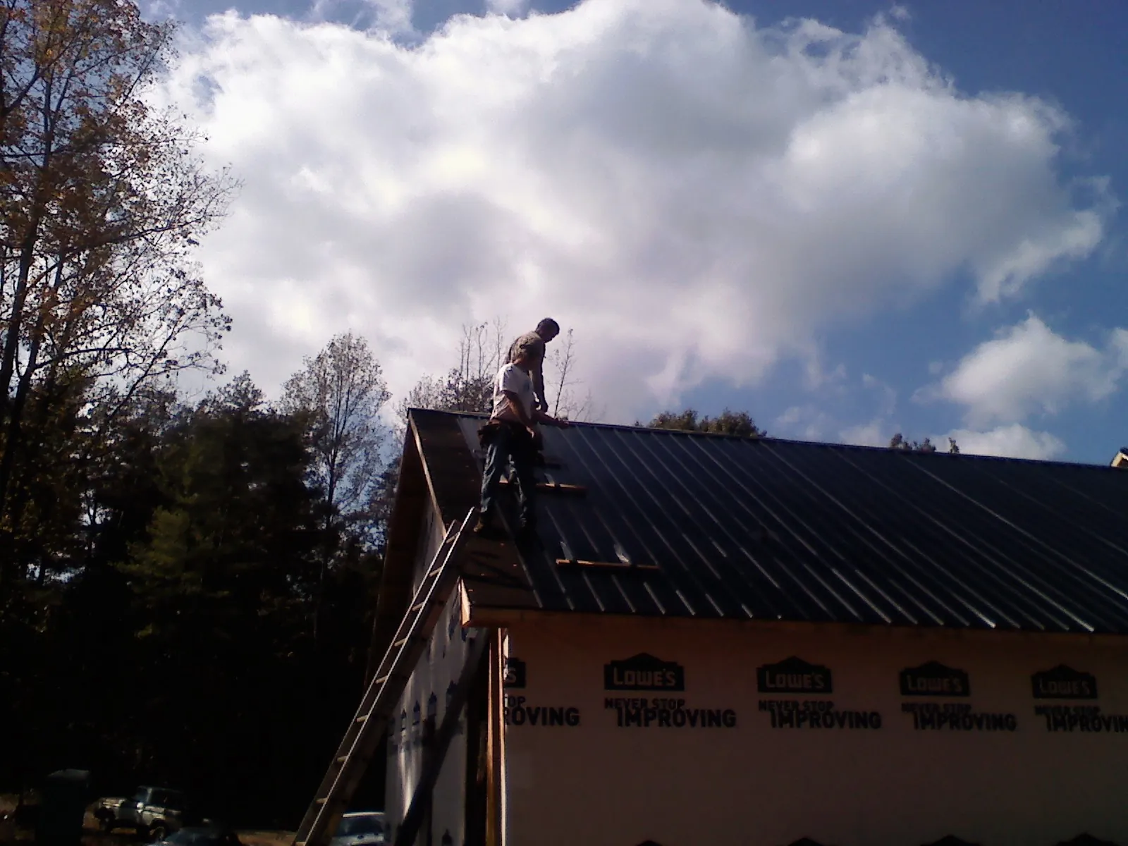 Roofer fastening dark metal panels high against a cloudy sky, from a Roof Inspection job in Smartsville