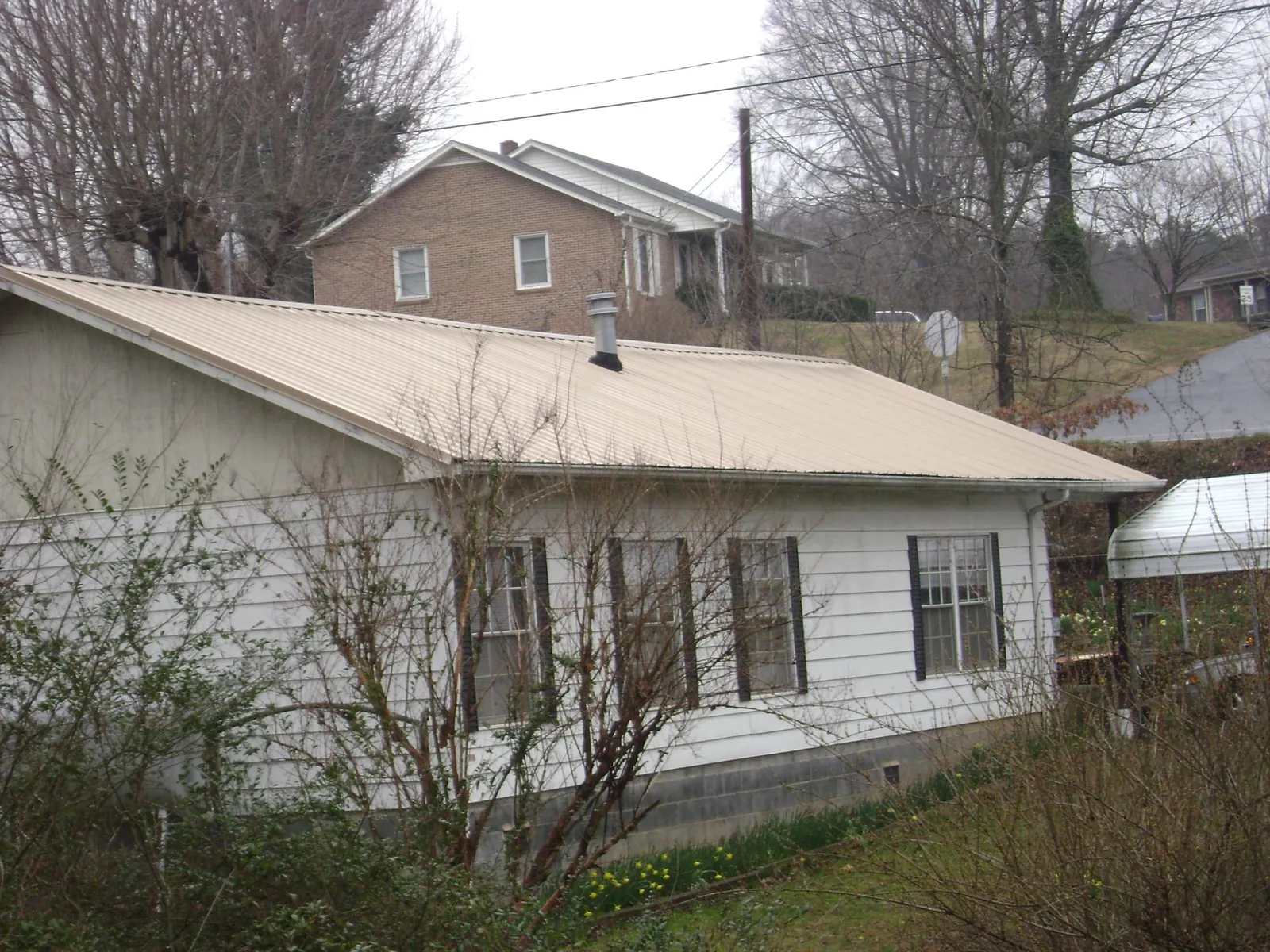Tan metal roof on a white sided house set into a hillside — Commercial Roofing by Roofing Brothers in Smartsville
